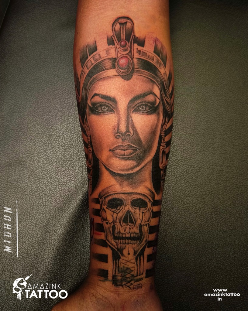 A detailed black and grey realism forearm sleeve tattoo combining a portrait of Egyptian Queen Cleopatra and an ancient pharaoh skull, done by Midhun at Amazing Tattoo in Kozhikode.